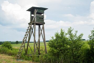 Wooden Hunters High Seat hunting tower on the green agriculture field. 