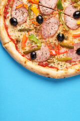 Close-up of Italian Pizza with homemade sausage, Mozzarella, Bulgarian pepper, Olives, Small cucumbers, Champignons, Oregano. Blue background. Copy Space