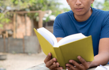 Hispanic man reading a yellow book. Latin student holding a book in his hands. Portrait of a brown...