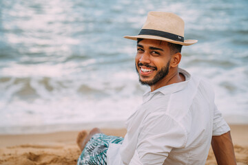 Silhouette of a young man on the beach. latin american man sitting on the beach sand, wearing a hat, looking at the camera. a beautiful summer day