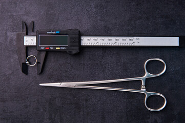Electronic caliper with piercing earring and clips. Lying on a black background. Piercing theme
