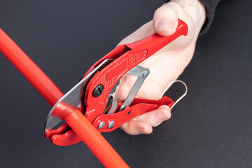 Man cuts the plastic pipe with manual pipe shears.