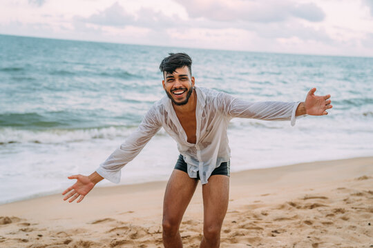 Friendly confident and smiling young latin american man with open arms looking at camera on the beach