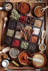 Top down view of an arrangement of various whole and ground spices on a wooden tray.