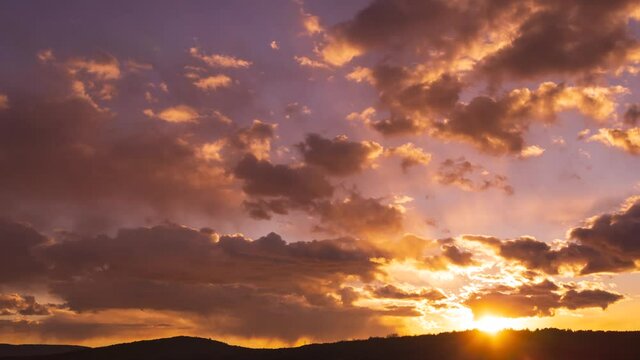 Sun rays through clouds timelapse. Sunset time lapse stock video in 4K. Beatiful anture cloudscape background. Evening dusk twilight light. Red, orange, yellow, purple, golden colors. Fast motion move