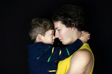The little boy looks gratefully at older brother, hugging him. The boy is grateful because his brother teaches him to play football, takes care of him while parents are at work