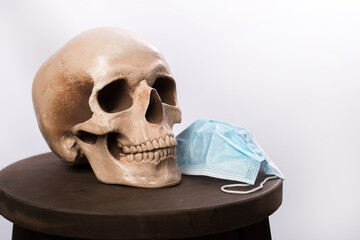 skull and medical mask lie on a wooden stand on a white background. place for text. coronavirus protection concept