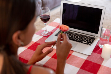 Caucasian woman sitting by desk having a video chat on laptop holding a flower and smiling