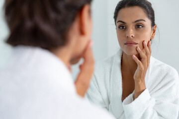 Obraz premium Caucasian woman wearing bathrobe standing in bathroom and lookig in mirror