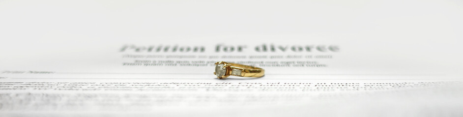 Conceptual wide image for divorce with two golden wedding rings in the middle and petition for divorce as background. Main focus on the rings. Blurred divorce contract papers with wedding jewelry.