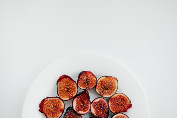 Ripe and sweet figs cut and arranged in a plate on a white background with free space. Fruits and vegetarianism