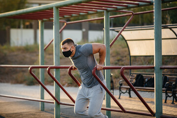 A young man does push-UPS, pull-UPS on a sports field in a mask during a pandemic at sunset. Sports, healthy lifestyle