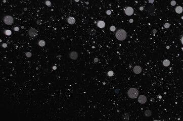 White snow falls at night on a black background.