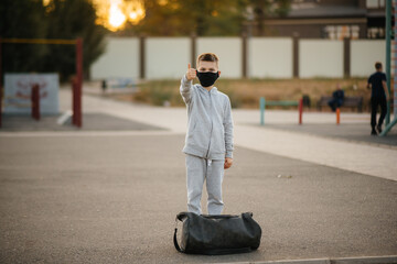 A boy stands on a sports field after an outdoor workout during sunset wearing a mask. Healthy lifestyle during the pandemic