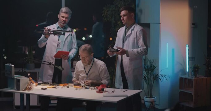 Trio of caucasian engineer specialists and young technician flying drone repairing microship of modern device with dolering equipment.
