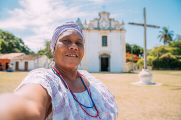 Happy Brazilian woman of African descent dressed in the traditional Bahian dress making a selfie in...