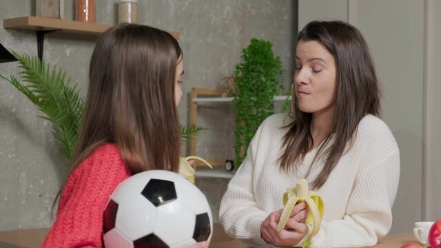 Happy mother talking to her daughter while they eat a banana