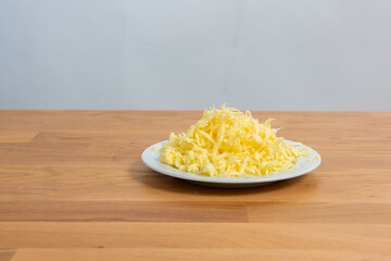 Plate of finely grated cheese on a wooden table..