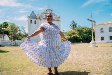 Happy Brazilian woman of African descent dressed in traditional Bahian dress dancing in front of...