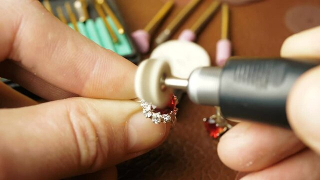The jeweler is engaged in cutting a precious stone on a gold ring.A professional jeweler polishes a red gem on a gold ring using a special tool.