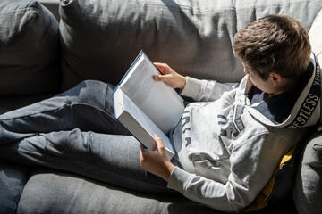 A young kid is reading a book in the sofa 