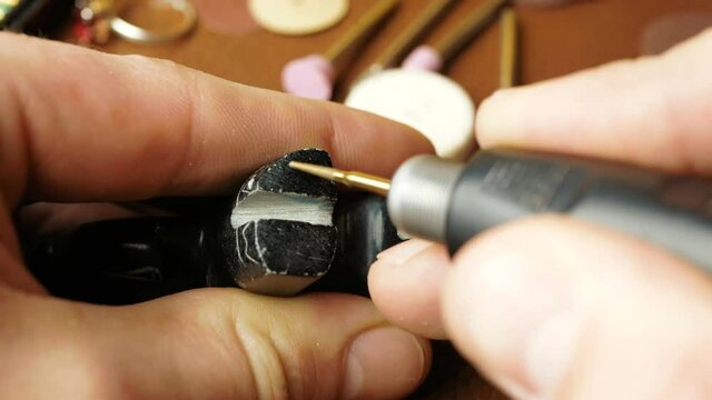 A professional jeweler engraves on a stone figurine to create a piece of jewelry. A professional engraver creates a piece of jewelry by making grooves with a special cutter.