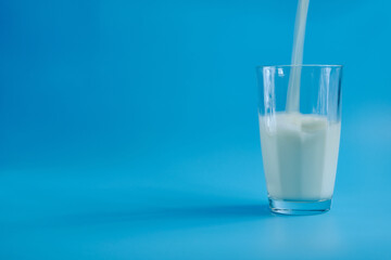 Transparent glass on a blue background and milk is poured into the glass