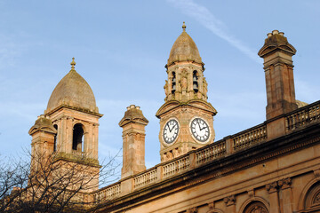 Fototapeta na wymiar Stone Towers & Clock on Old Stone Public Building against Blue Sky