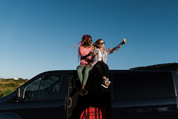 Multiracial girls cheering with wine outdoors in camper van while taking selfie with smartphone - Focus on faces