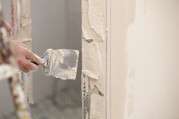 Builder using a trowel to add plaster. Plastering wall with putty-knife, close up image. Fixing...