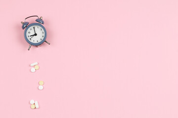 Alarm clock and pills on a pink background. Schedule.
