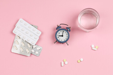 Alarm clock, glass of water and pills on a pink background. Schedule.
