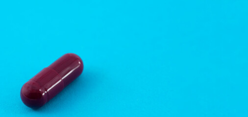 one burgundy pill close up, with copy space on a blue background. Pharmacy