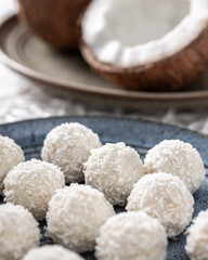 Portions of white chocolate coconut candy balls on the plate and cracked coconut on the background,...