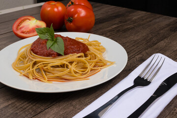 Pasta with sugo sauce and basil leaves. Whole red tomatoes. Tomato sliced ​​in half at the bottom. Cutlery on napkin. Popular food photography.