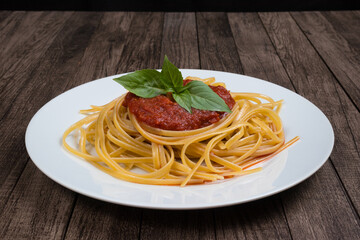 Pasta with sugo sauce and basil leaves served on a white plate. Photography with centralized elements. Italian gastronomy.