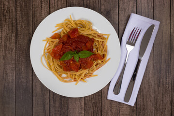 Pasta with rustic tomato sauce and basil leaves. Bavette pasta in red sauce. Top shot with centralized elements. Fork and knife on napkin.