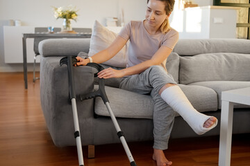 Woman in her late twenties on couch at home with elbow crutches and orthopedic plaster. Fracture of...