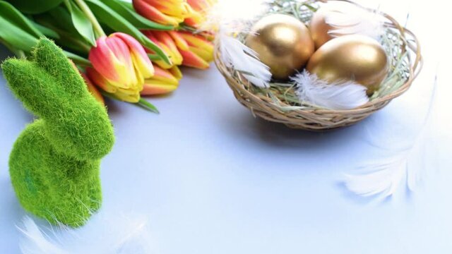 Easter eggs basket. Golden egg in basket with spring tulips, white feathers on pastel blue background in Happy Easter decoration. Traditional decoration in sun light