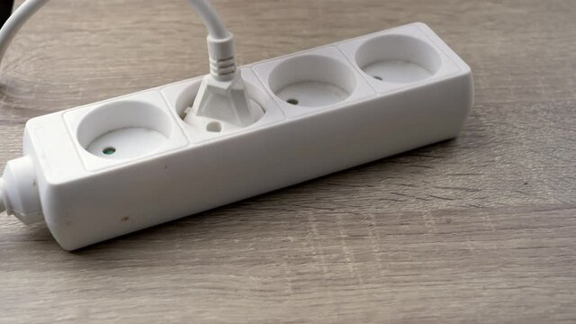A close-up of a man's hand connecting a plug to a white extension cord to generate electricity.