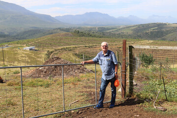 Fototapeta na wymiar Elderly South African farmer with his newly planted macadamia nut orchard in the far background