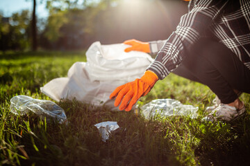 A woman collects and puts used plastic bottle into a trash bag. A volunteer cleans up the park on a...