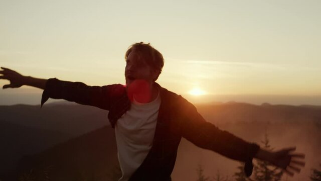 Man dancing in mountains at sunset. Happy guy gesturing hands during dance