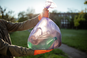 Young man volunteer hold a trash bag in his hands outdoors. A volunteer cleans up the park on a sunny bright day. Clearing, pollution, ecology and plastic concept.