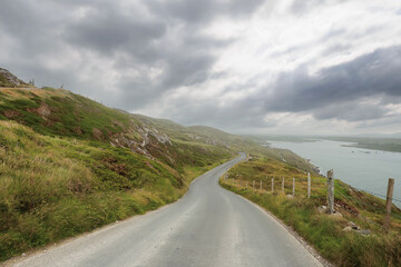 Small narrow asphalt road with beautiful unique views, Sky road loop near Clifden town, county Galway, Ireland. Cloudy sky. Irish scenery. Nature landscape. Popular tourist travel destination