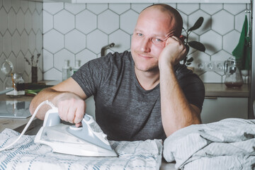 Man smiles ironing bed linen. Father is engaged in household chores.