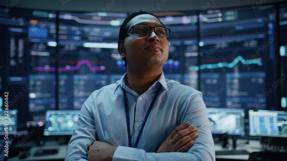 Poster Portrait of Professional Indian IT Technical Support Specialist or Software Developer Posing in Front of Camera in a Modern Monitoring Control Room Full of Computer Displays with Technological Data.