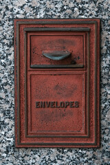 Red metal mail drop box on an exterior marble wall