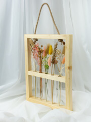 Flower arrangement of dried flowers in narrow glass vases in a natural wooden frame. Pink, yellow, beige, white colors