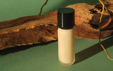 Blank bottle of foundation for makeup on sunny summer green background with eye shadow and wooden...